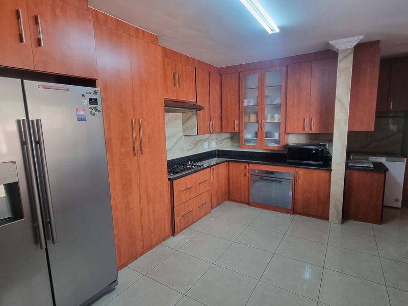 A spacious kitchen featuring warm-toned wooden cabinetry, granite countertops, a gas hob, built-in oven, and tiled flooring with ample storage space.