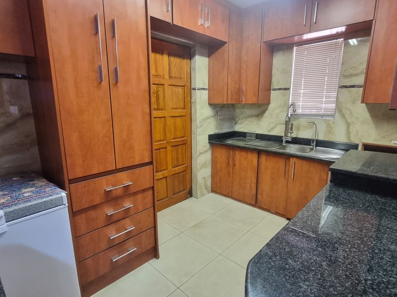 A functional kitchen featuring warm-toned wooden cabinetry, dark granite countertops, tiled flooring, and a stainless steel sink with a modern mixer tap.