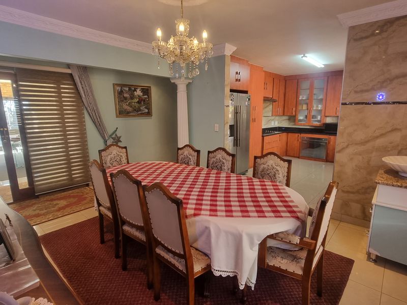 Open-plan dining and kitchen area featuring wooden cabinetry, built-in appliances, a decorative chandelier, and direct access to an outdoor patio through sliding glass doors.