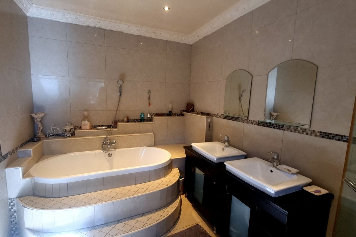 A spacious bathroom featuring a raised built-in bathtub, double vanity with modern sinks, and floor-to-ceiling tiling with decorative mosaic accents.