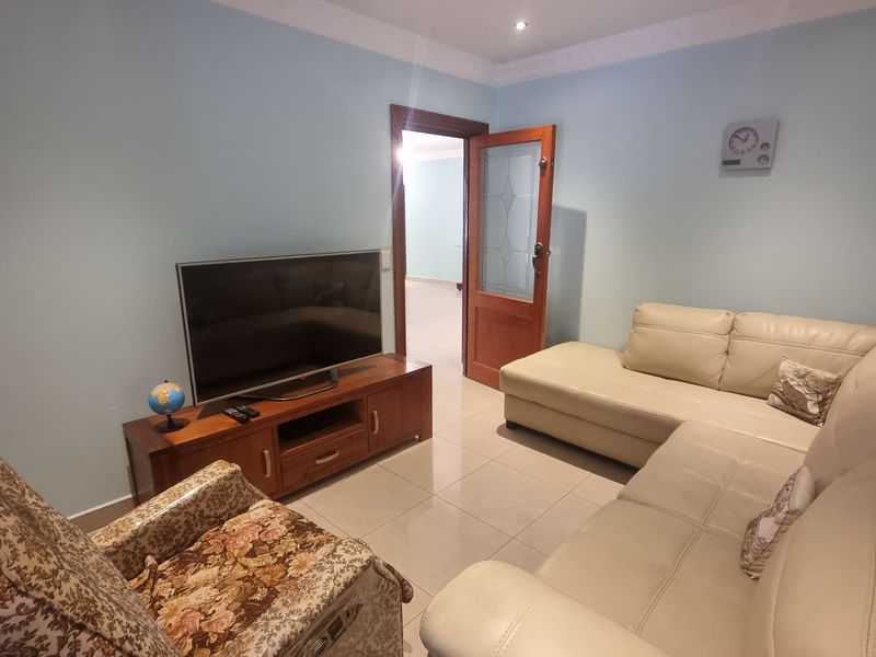 A comfortable living room featuring tiled flooring, decorative ceiling cornicing, and a timber-framed glass panel door leading to an adjacent space.