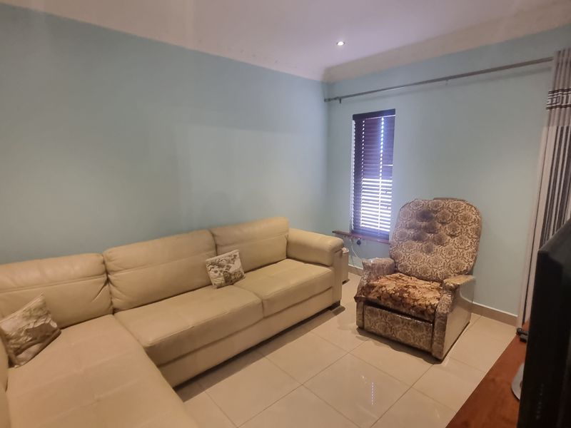 A living room featuring light blue walls, tiled flooring, and recessed downlighting, providing a functional and neutral space.