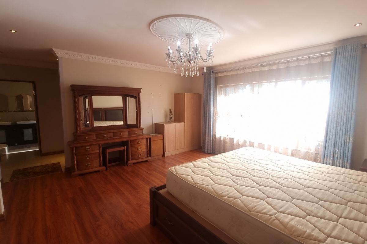 Spacious bedroom featuring laminate flooring, decorative ceiling rose with chandelier, and built-in cupboards, with an en-suite bathroom visible through the doorway.