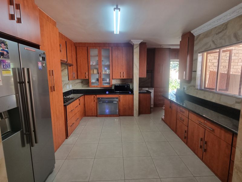 Spacious kitchen featuring extensive wooden cabinetry, granite countertops, built-in oven and hob, and neutral tiled flooring.
