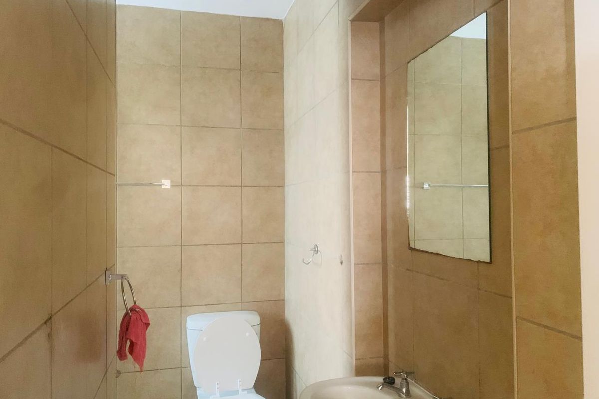 A functional bathroom featuring neutral ceramic wall tiles, a pedestal basin, and a wall-mounted mirror.