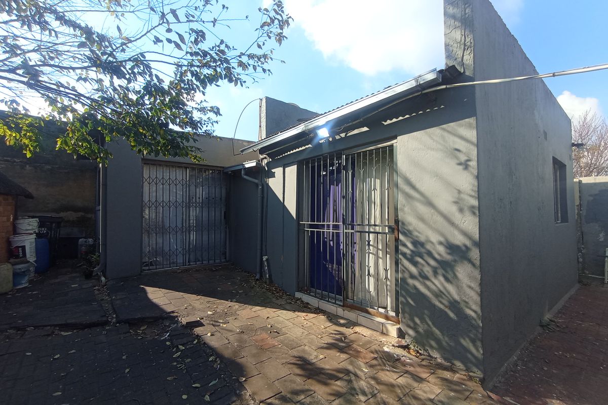 Rear exterior view of the property featuring paved courtyard area, security gates, and painted masonry walls.