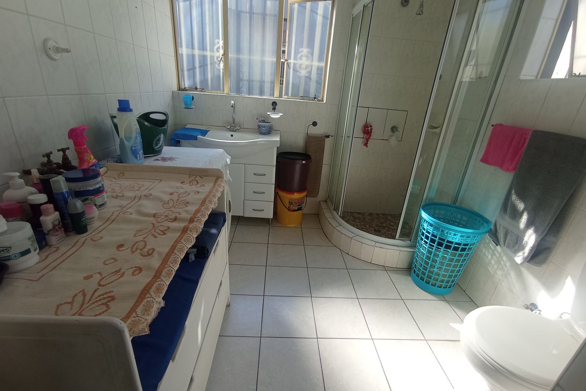 A functional bathroom featuring a corner shower enclosure, vanity basin, and toilet with tiled flooring and walls.