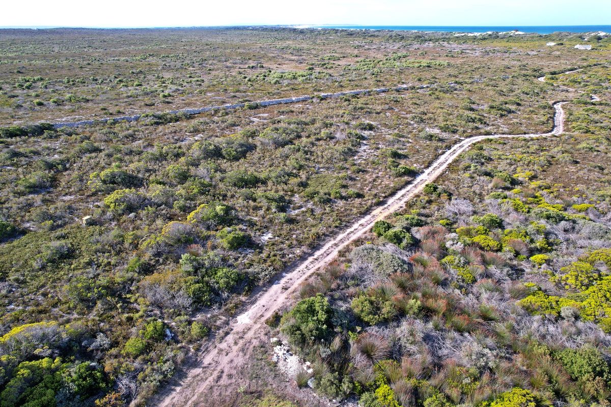 Aerial view of a large vacant residential plot featuring natural coastal vegetation, an unpaved access track, and distant ocean views.