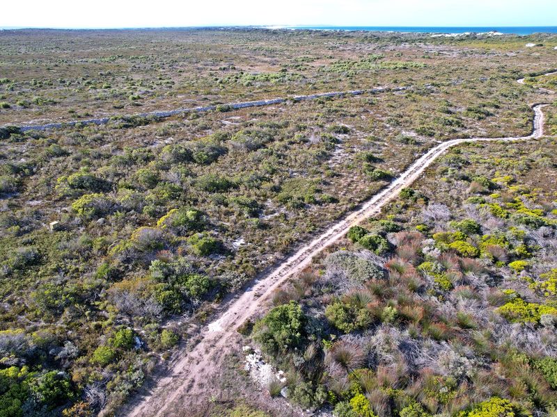 Aerial view of a large vacant residential plot featuring natural coastal vegetation, an unpaved access track, and distant ocean views.