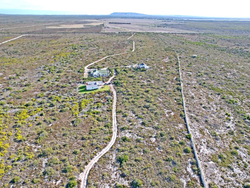 Aerial view of a large residential land plot featuring natural vegetation, gravel access roads, and existing residential structures.