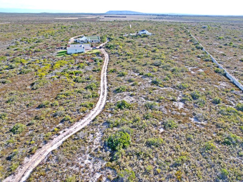 Aerial view of a large vacant residential plot featuring natural vegetation, an unpaved access road, and existing boundary walling.