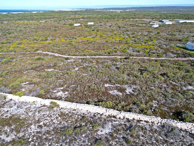 Aerial view of a large vacant residential plot featuring natural coastal vegetation, a stone boundary wall, and an unpaved access track.