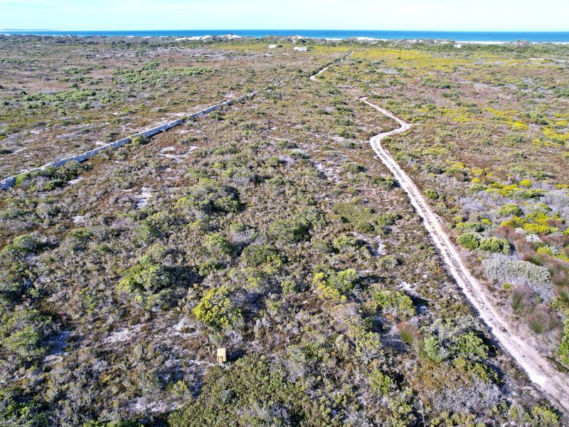 Aerial view of a large vacant residential plot featuring natural coastal vegetation, a dirt access road, and a stone boundary wall.