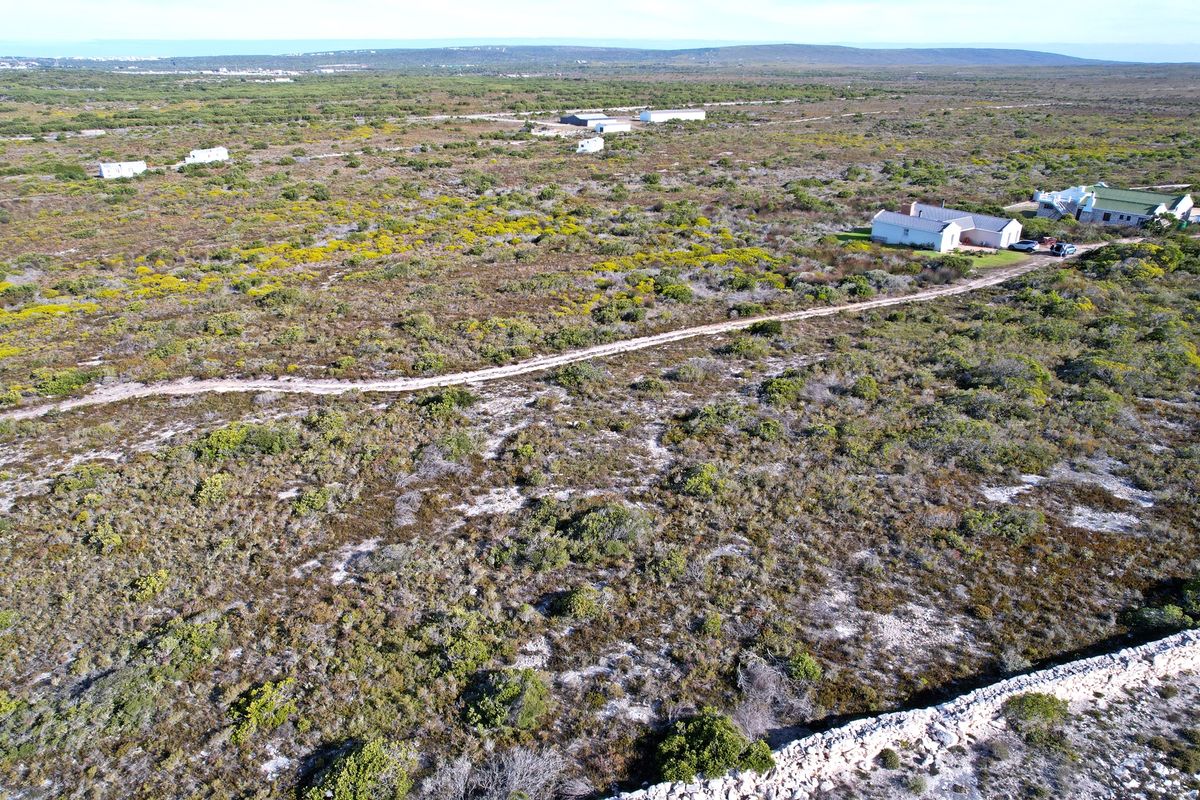 Aerial view of a large residential vacant land plot featuring natural vegetation, a dirt access road, and a stone boundary wall.