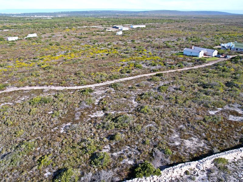 Aerial view of a large residential vacant land plot featuring natural vegetation, a dirt access road, and a stone boundary wall.