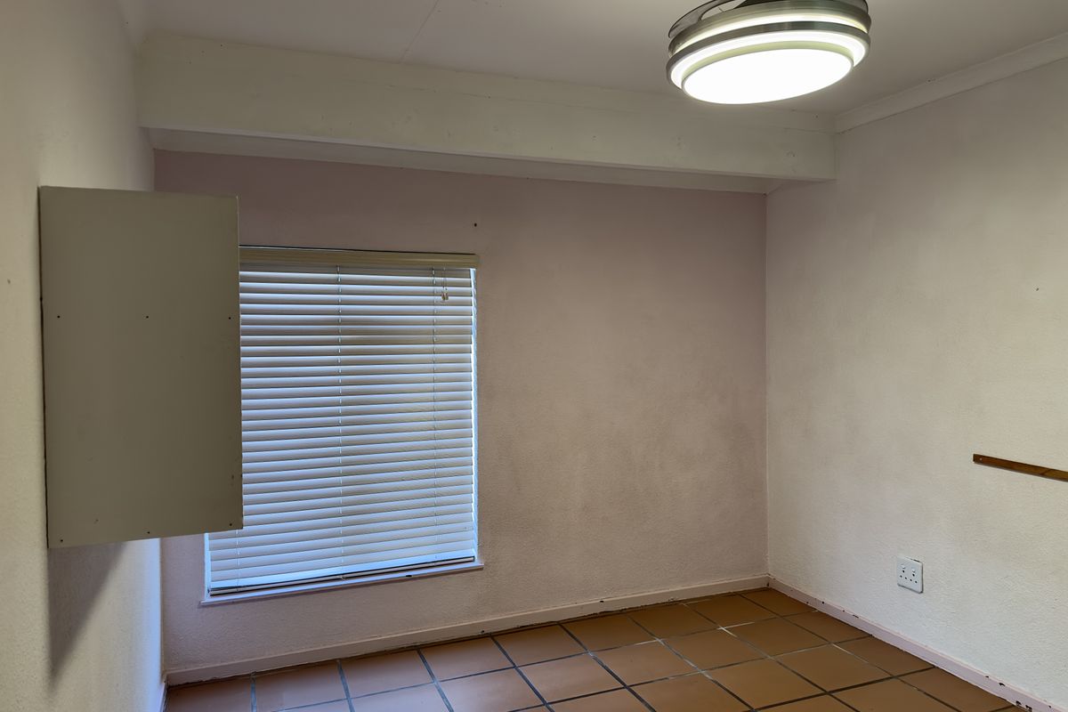 An empty bedroom featuring tiled flooring, a ceiling fan, and venetian blinds, requiring cosmetic updates to the wall finishes.