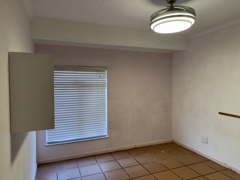 An empty bedroom featuring tiled flooring, a ceiling fan, and venetian blinds, requiring cosmetic updates to the wall finishes.