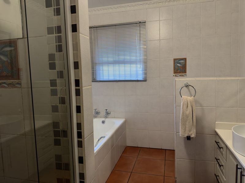 A functional bathroom featuring a built-in bathtub, separate shower enclosure, and a vanity with a vessel sink, finished with neutral wall tiles.