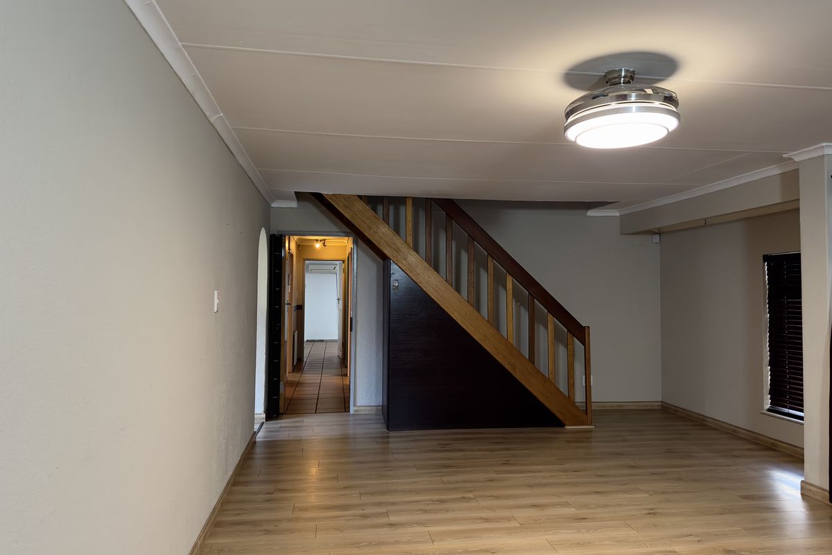 An empty living room featuring laminate flooring, a wooden staircase, and neutral wall finishes, providing a clean and versatile space.