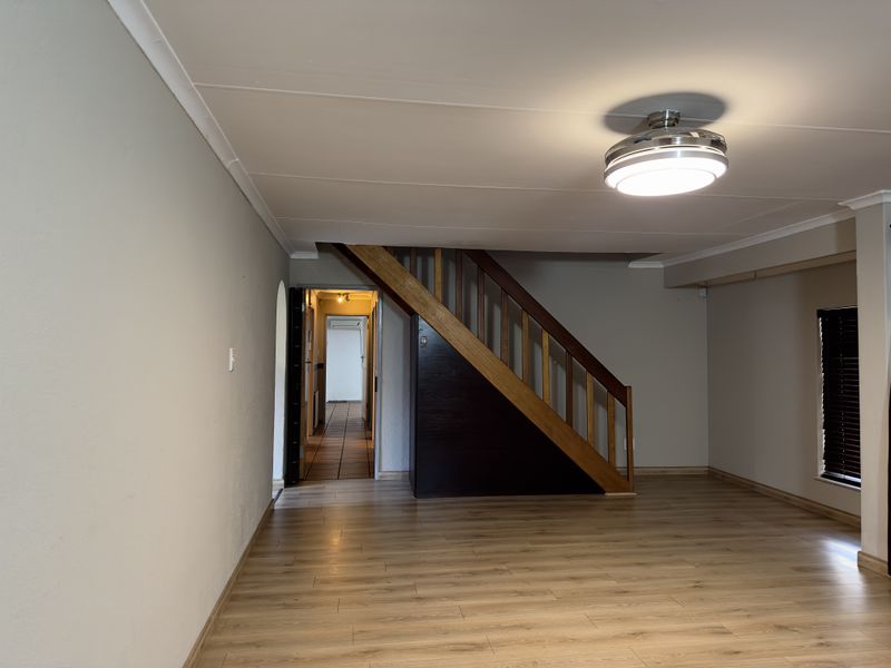 An empty living room featuring laminate flooring, a wooden staircase, and neutral wall finishes, providing a clean and versatile space.