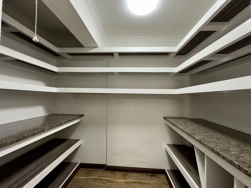 A clean, empty walk-in pantry or scullery featuring extensive built-in shelving and durable laminate countertops.