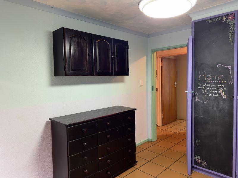 A hallway area featuring tiled flooring and a doorway leading to an adjacent room, with wall-mounted cabinetry and a chalkboard door finish.