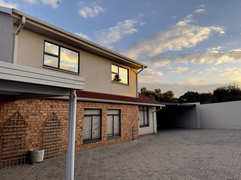 A well-maintained two-story residential property featuring a brick and plaster facade, tiled roof, and a spacious paved driveway with an integrated carport.