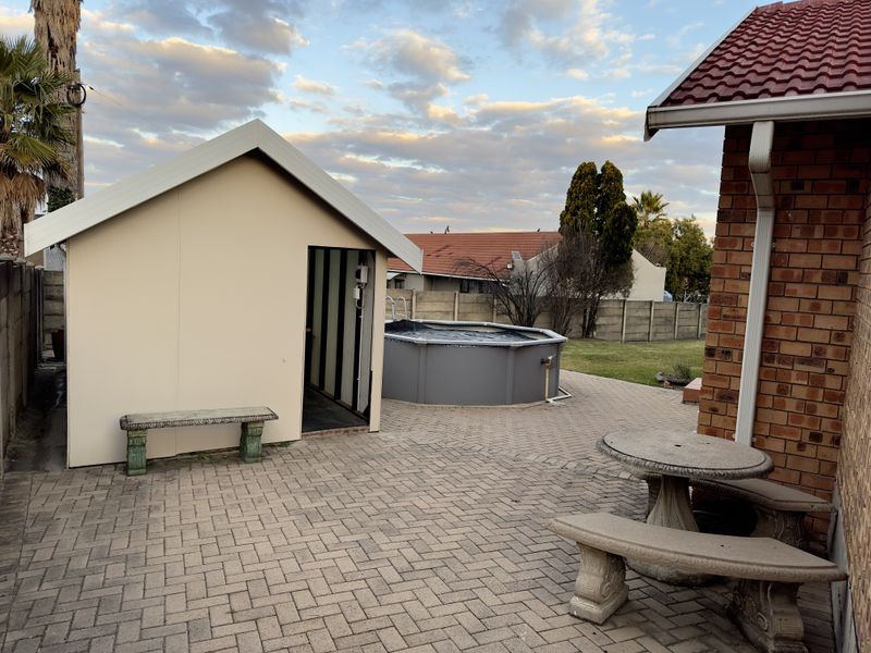 Rear garden area featuring a paved patio, an above-ground swimming pool, and a detached utility shed adjacent to the main brick dwelling.