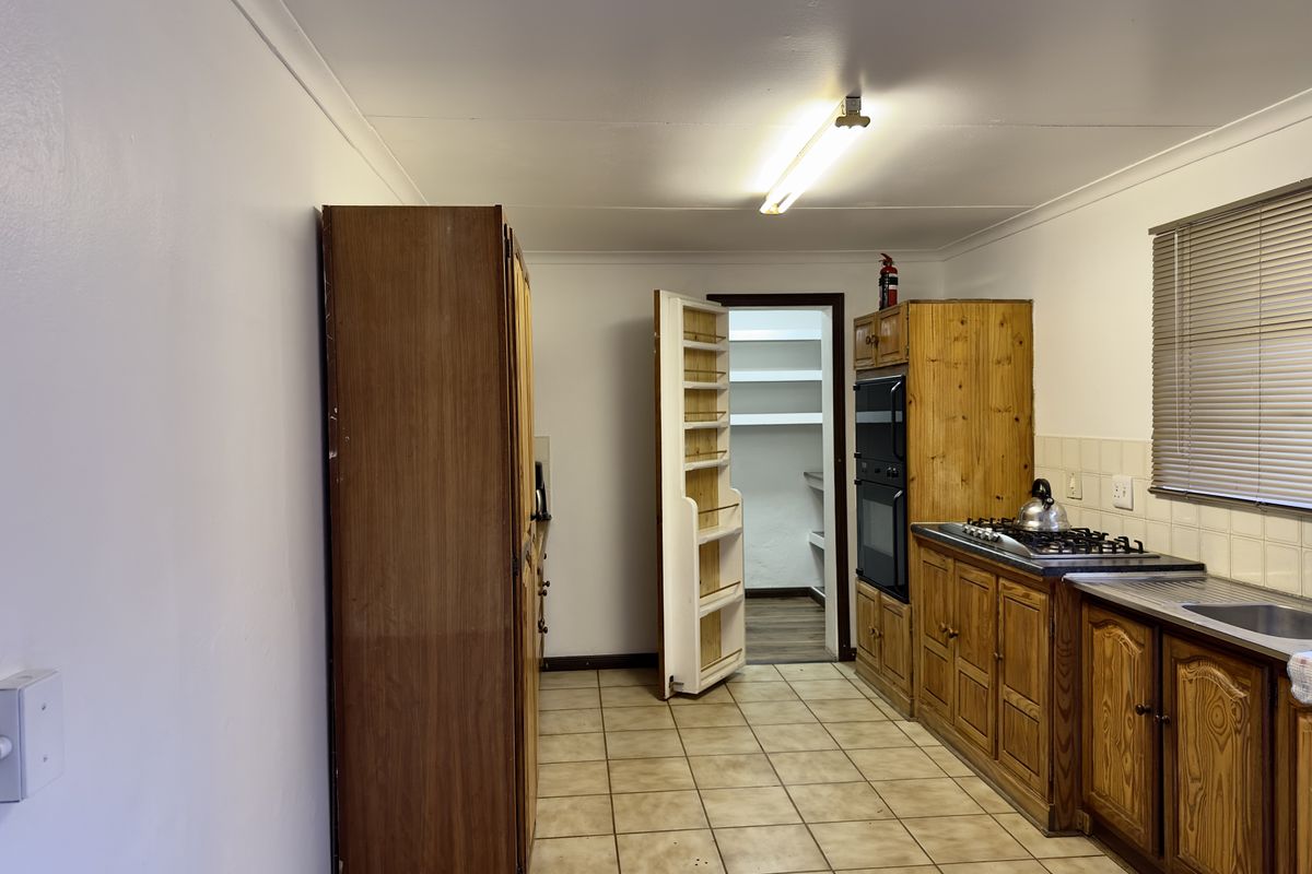 A functional kitchen featuring wooden cabinetry, a gas hob, built-in oven, and an adjoining walk-in pantry with tiled flooring throughout.