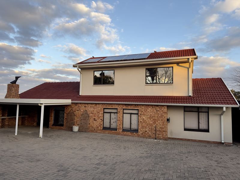 Rear view of a two-story house featuring a brick and rendered facade, tiled roof with solar panels, and a paved courtyard area.