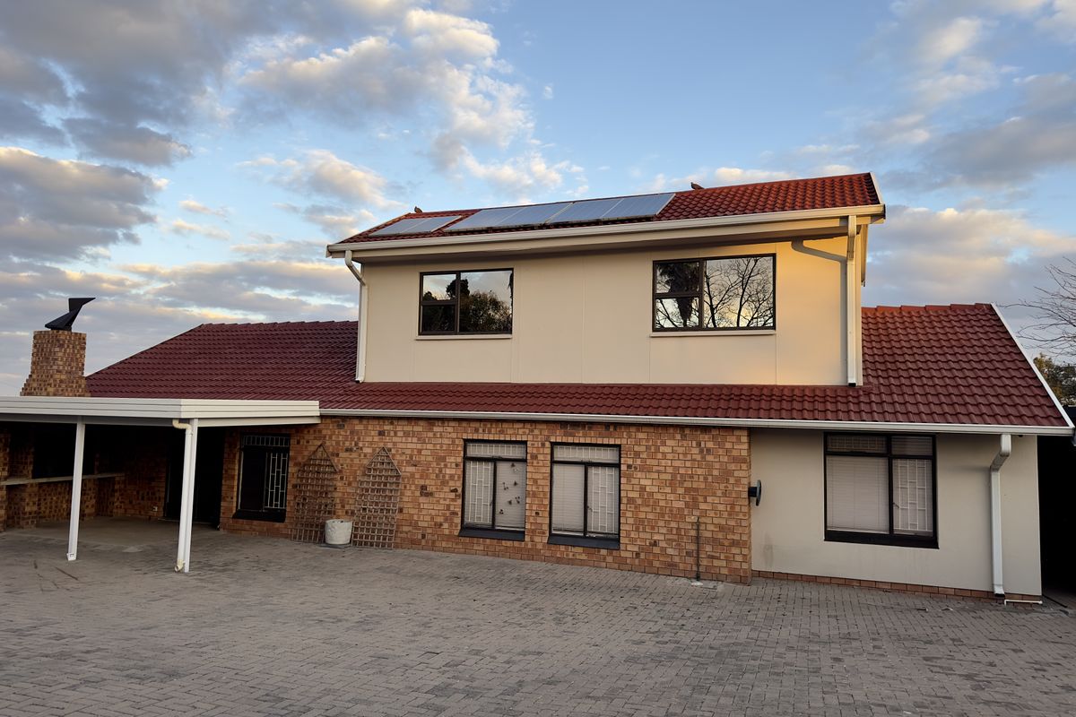 Rear view of a two-story house featuring a brick and rendered facade, tiled roof with solar panels, and a paved courtyard area.