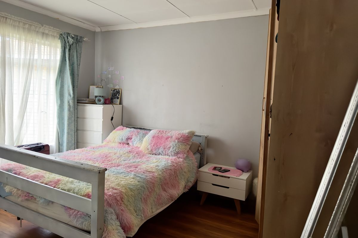A standard bedroom featuring wood-look flooring, a large window with natural light, and built-in wardrobe storage.