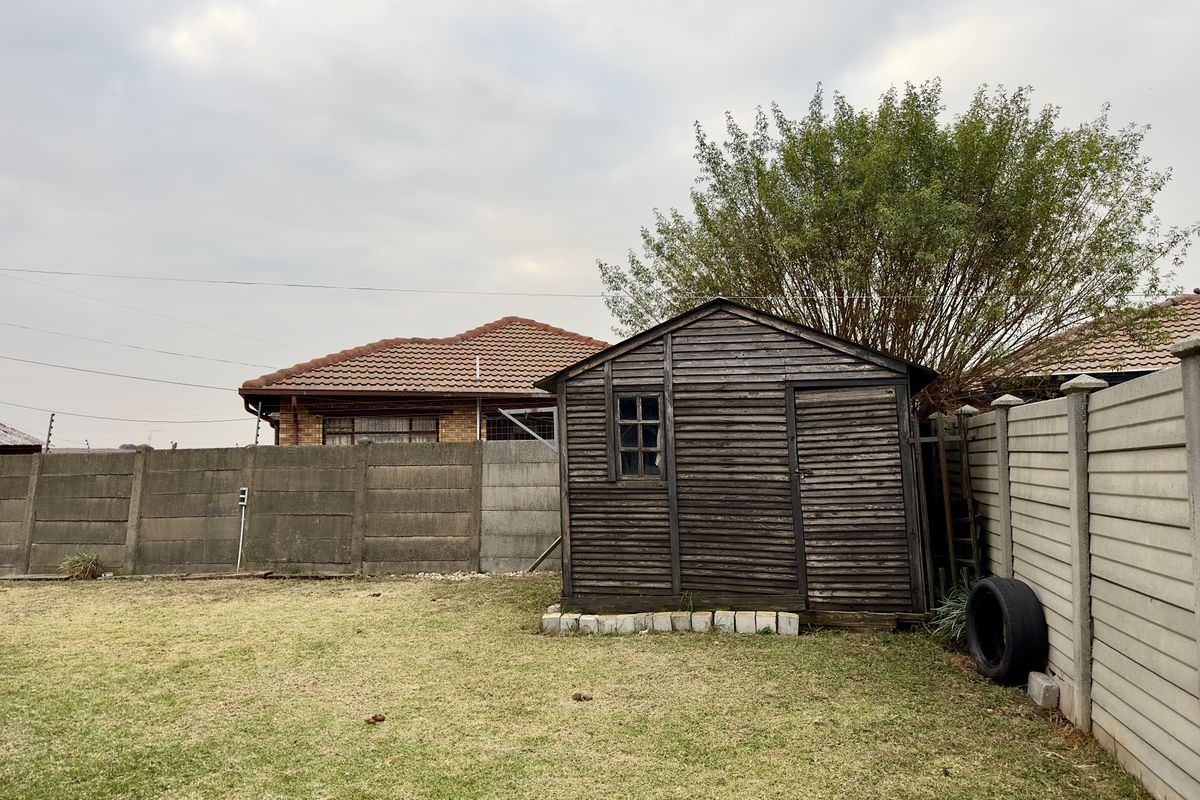 A backyard view featuring a weathered wooden garden shed situated on a lawn, enclosed by precast concrete boundary walls.
