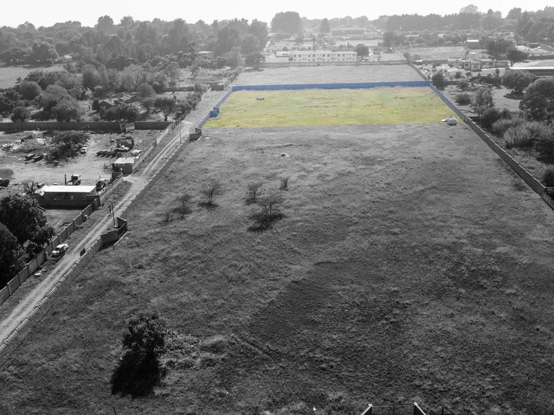 An aerial view of a large, vacant residential plot of land, enclosed by perimeter walls and fencing in a suburban setting.