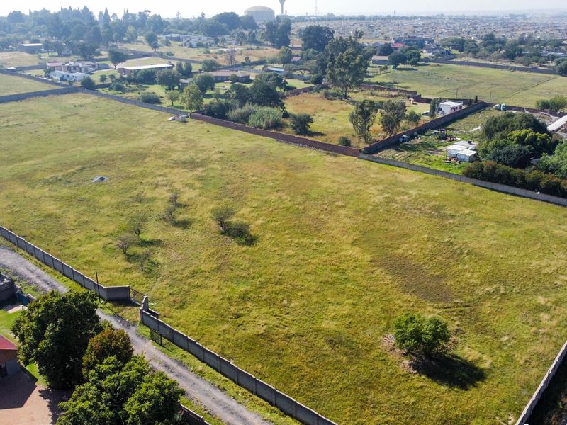 An aerial view of a large, vacant residential plot enclosed by perimeter walls, featuring open grass land and established boundary fencing.