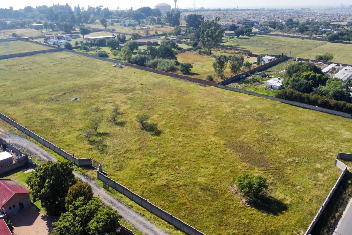 An aerial view of a large, vacant residential plot enclosed by perimeter walls, featuring open grass land and established boundary fencing.