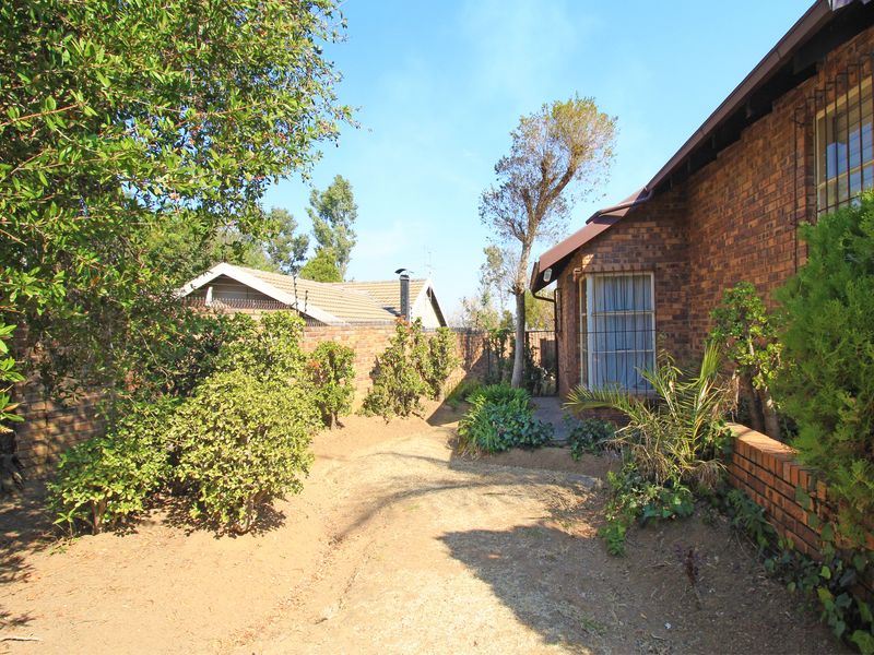 A view of the rear garden area featuring face brick exterior walls, security bars on windows, and a paved pathway along the side of the house.
