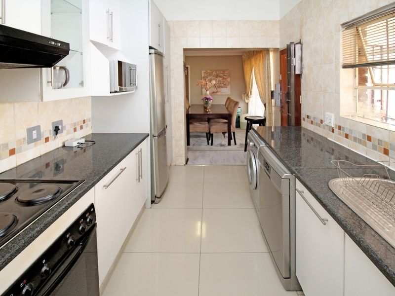 A functional galley-style kitchen featuring granite countertops, built-in appliances, tiled splashbacks, and modern floor tiles, leading through to the dining area.
