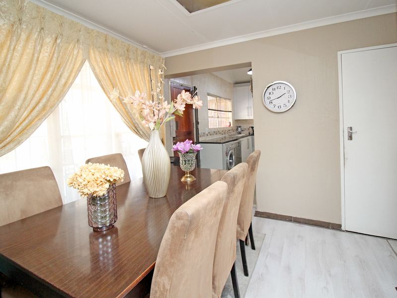 Open plan dining area featuring light laminate flooring and coved ceilings, with a direct view into the adjacent kitchen space.