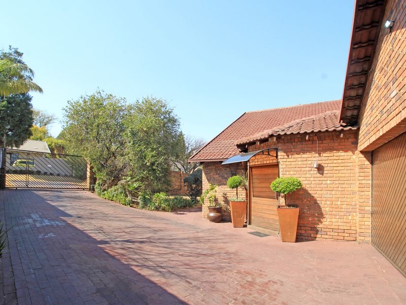 A well-maintained front exterior featuring a brick driveway, facebrick facade, and a secure gated entrance with a tiled roof garage.