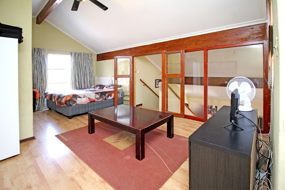 Spacious bedroom featuring vaulted ceilings with exposed timber beams, laminate flooring, and a unique timber-framed glass partition overlooking the staircase area.