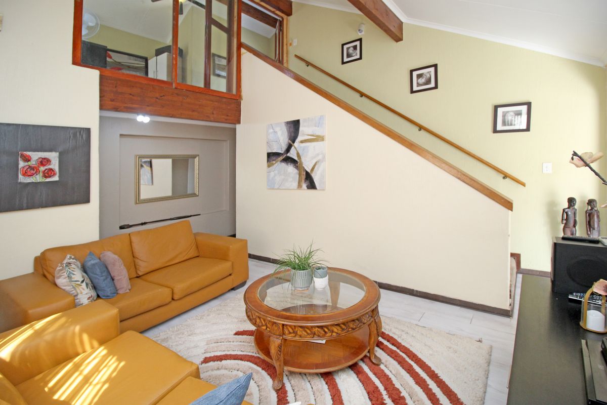 Spacious living area featuring high ceilings with exposed timber beams, a staircase with a timber handrail, and a mezzanine level with glass balustrade.