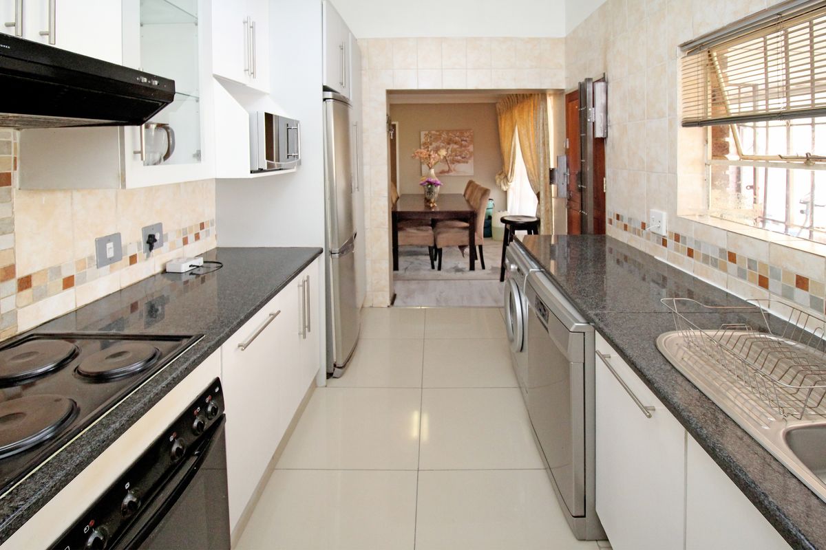 A functional galley-style kitchen featuring granite countertops, built-in appliances, tiled splashbacks, and modern floor tiles, leading through to the dining area.