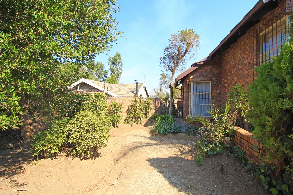 A view of the rear garden area featuring face brick exterior walls, security bars on windows, and a paved pathway along the side of the house.