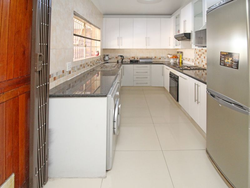 Modern kitchen featuring white cabinetry, granite countertops, tiled backsplash, and integrated appliances, offering a clean and functional workspace.