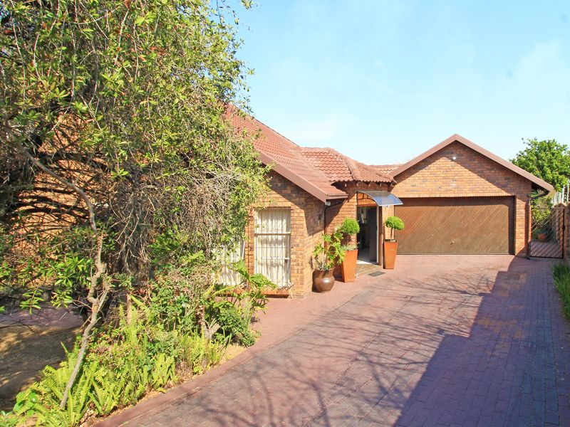Front view of a brick house featuring a tiled roof, a paved driveway, and an integrated double garage with a wooden door.