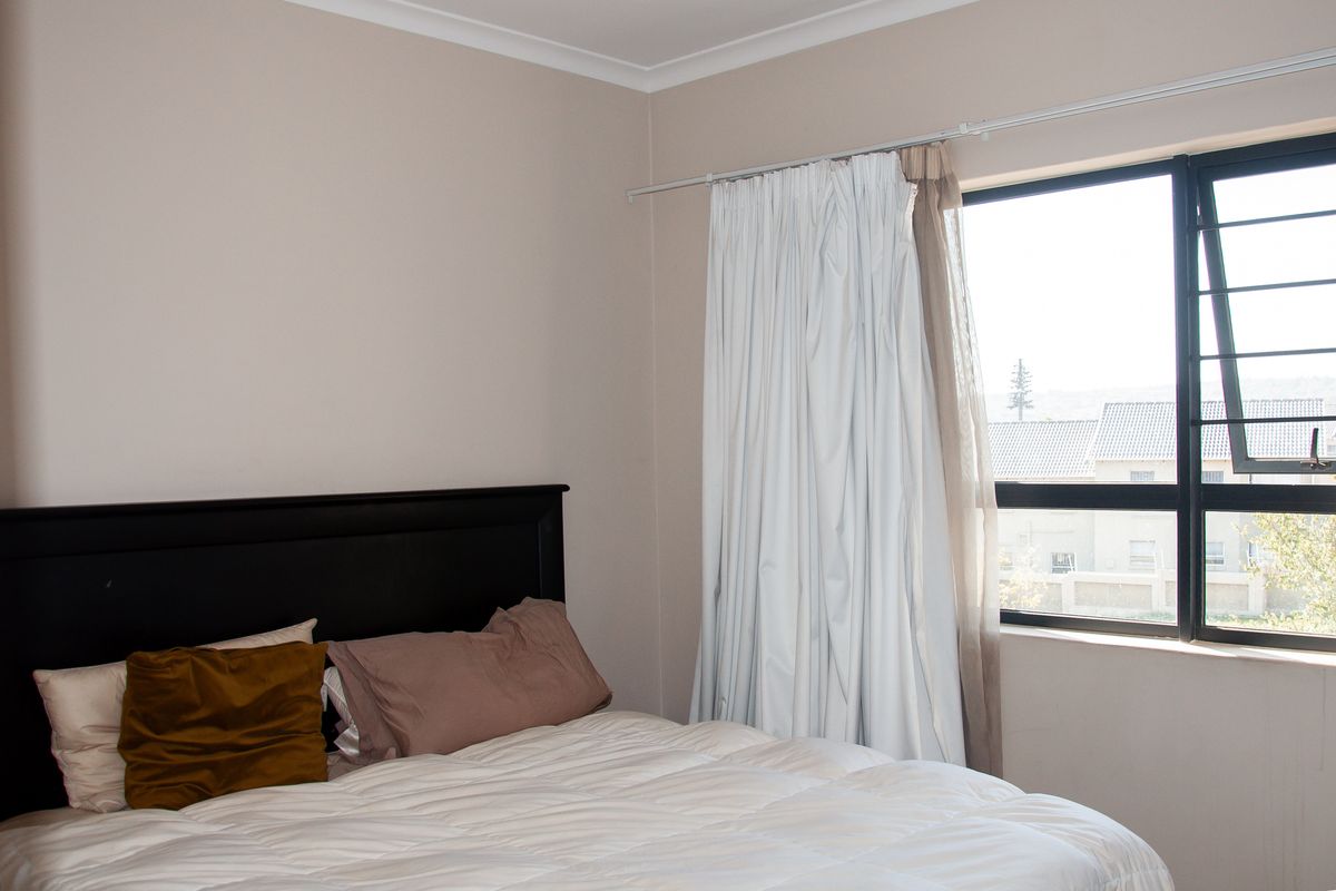 A bedroom featuring neutral wall tones, a large window with integrated security bars, and curtain tracks.