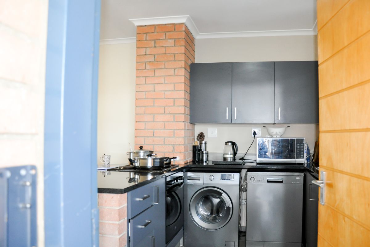 Compact kitchen featuring dark cabinetry, granite countertops, a brick feature pillar, and integrated space for a washing machine and dishwasher.