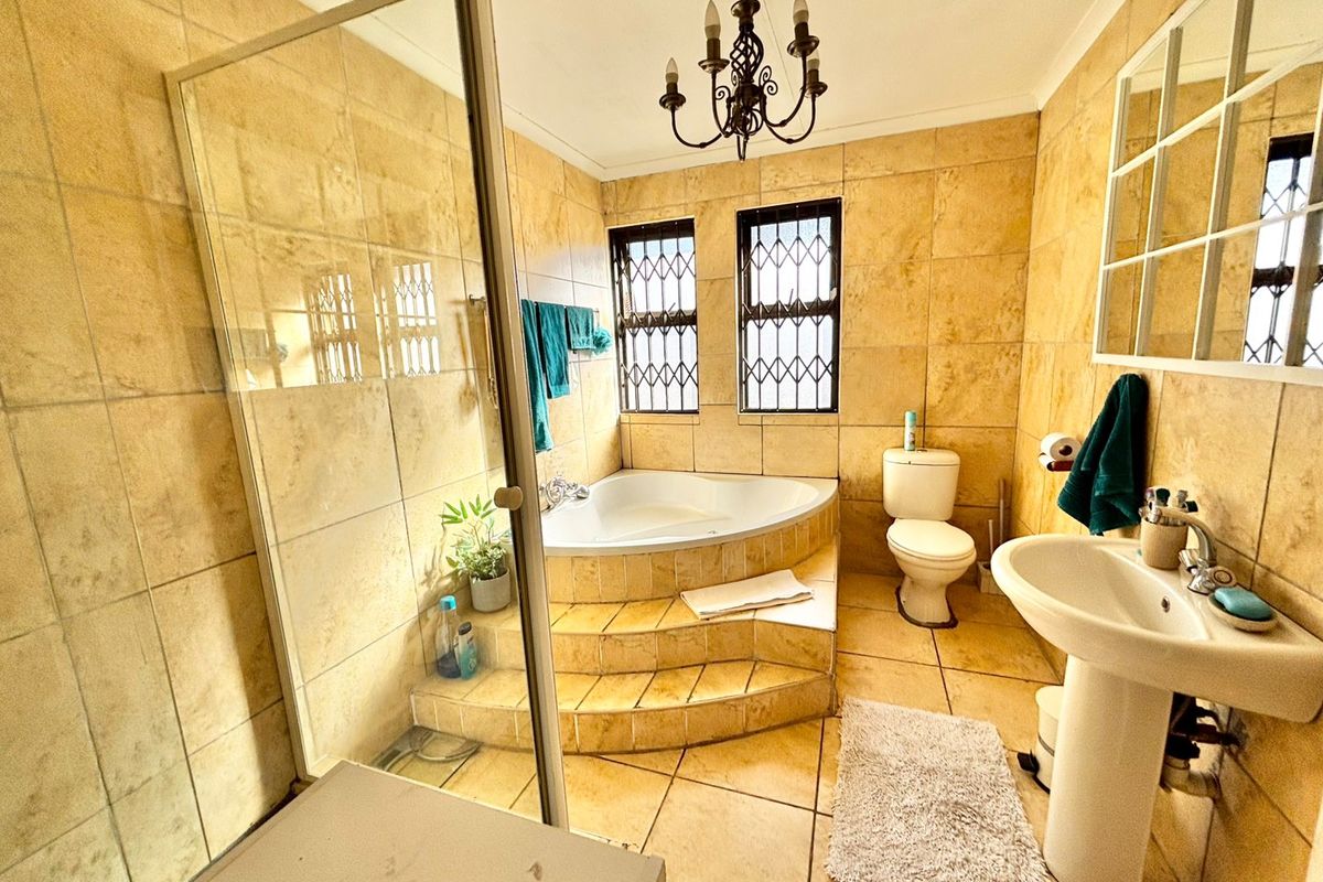 A dated bathroom featuring a corner bathtub on a raised platform, a glass-enclosed shower, pedestal basin, and full-height wall tiling.