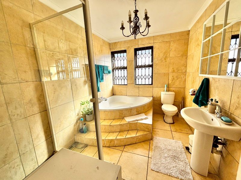 A dated bathroom featuring a corner bathtub on a raised platform, a glass-enclosed shower, pedestal basin, and full-height wall tiling.